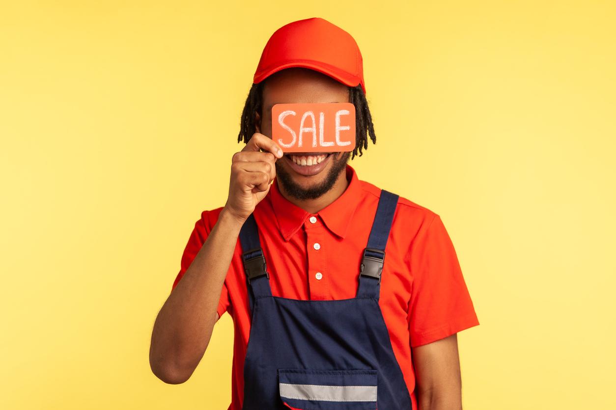Unknown male worker standing covering eyes with card with sale inscription, service industry.