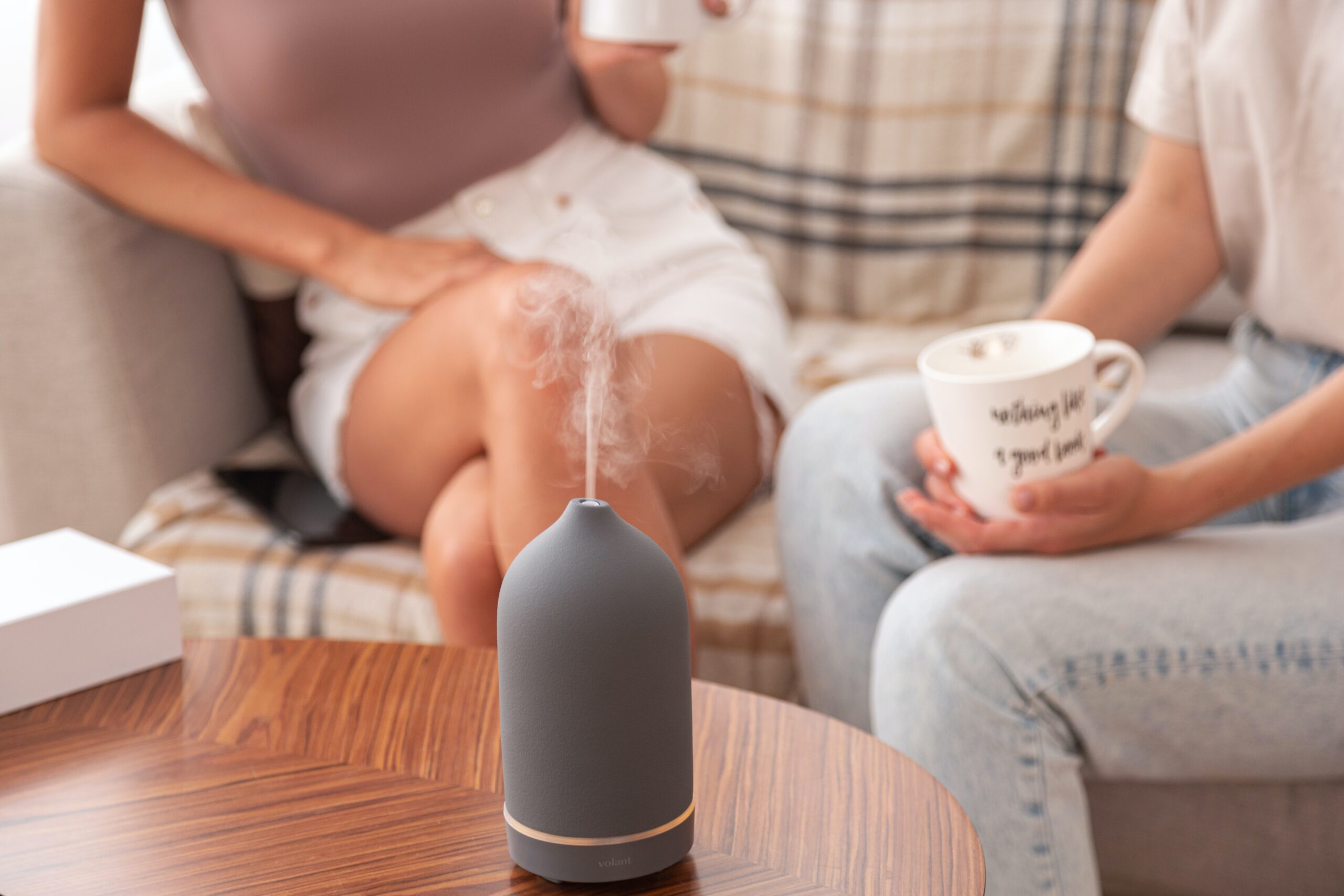 A table with an air purifier on it and two people in the background drinking out of coffee mugs
