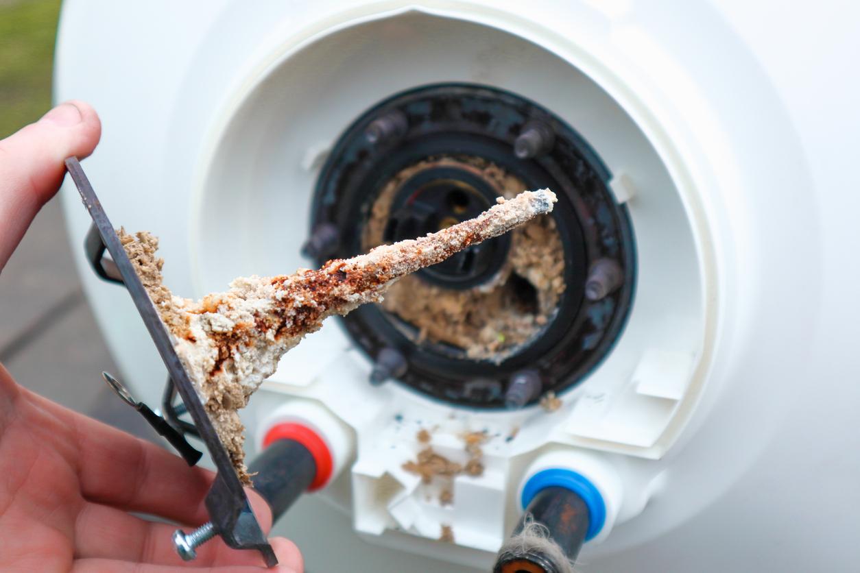 Water heater repair. Repair and maintenance of boilers. The master plumber pulls out a tubular electric heater covered with lime scale from the hole in the boiler.