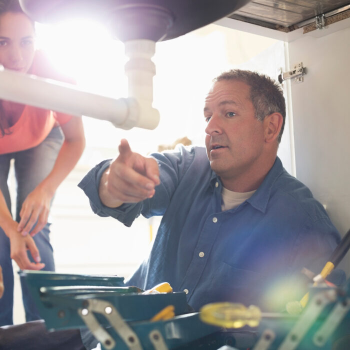 Plumbers working on pipes under sink